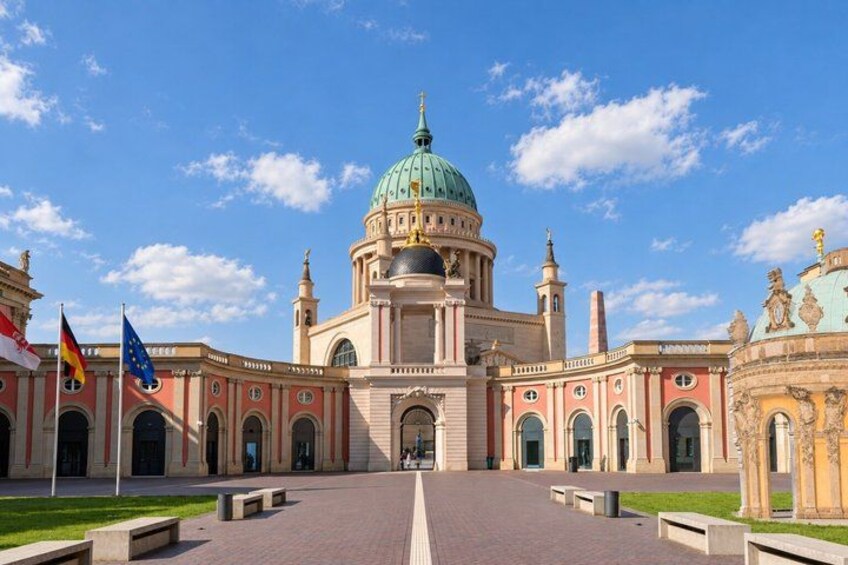 A large historic building with a prominent dome, flags, and a paved courtyard. 5