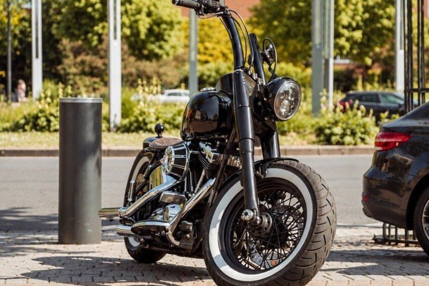 A black motorcycle parked on a paved surface with a black car in the background. 4