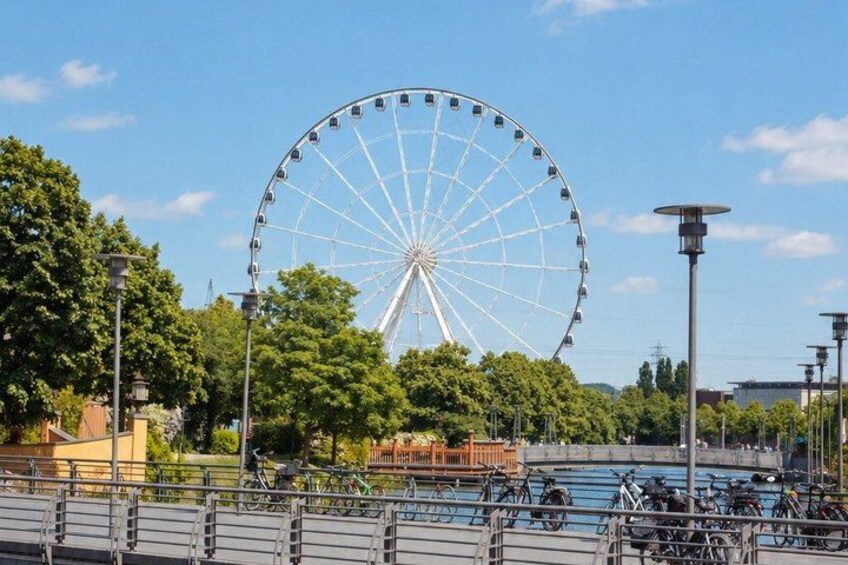 A large Ferris wheel, bicycles, and a park with trees and a body of water. 5