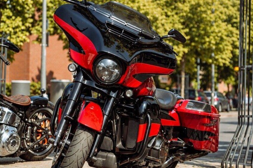 A red and black motorcycle parked on a sidewalk with a basket attached to the rear. 3