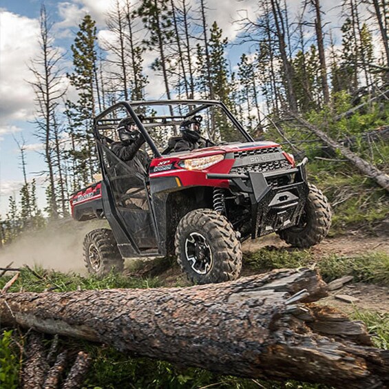 A red off-road vehicle navigating a forest trail with a driver and passenger. 4