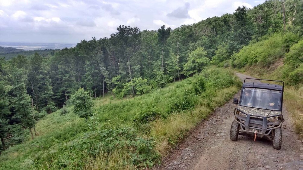 A 4x4 vehicle on a dirt path surrounded by dense forest. 1