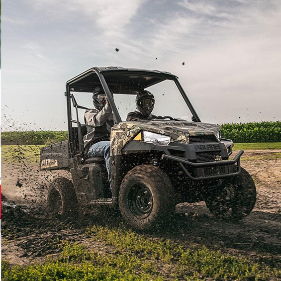 A four-wheeled vehicle with a raised front bumper and a windshield, driving through a muddy field with water splashing around. 2