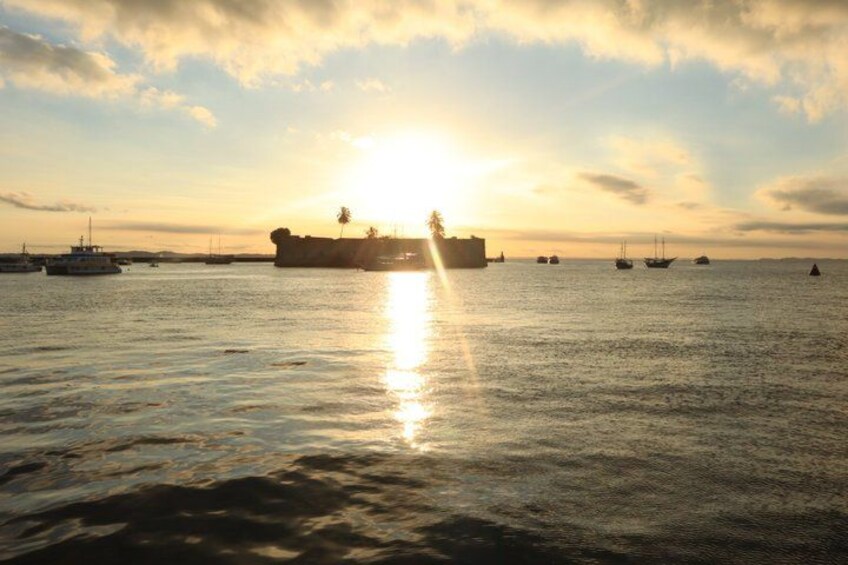 A sunset over a calm sea with several boats and a large ship in the distance. 3