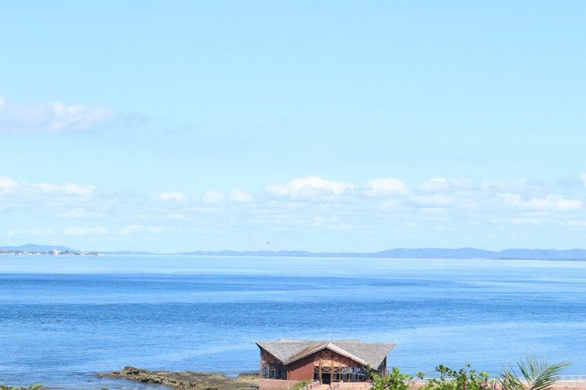 A coastal scene with a small building near the shore, calm sea, and distant landforms. 5