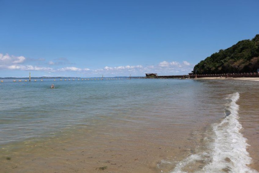 A beach with clear water, a sandy shore, and a distant hill. 4