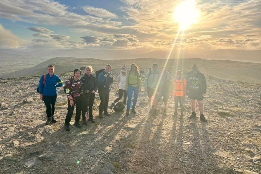A group of people standing on a rocky terrain with a sunset in the background. 1