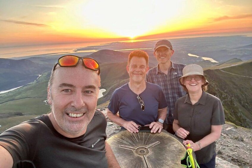A group of people on a mountain with a sunset in the background. 4