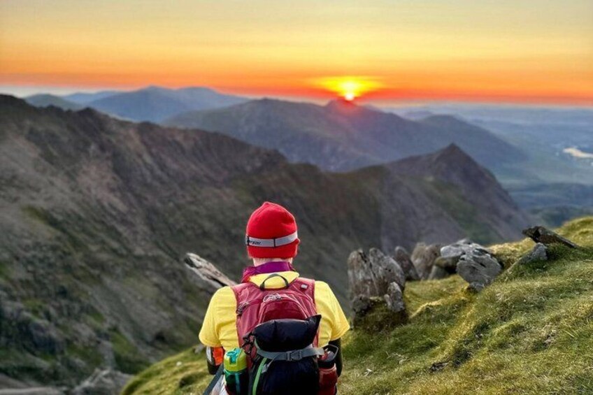 A hiker with a red hat and yellow jacket on a mountain trail. 5