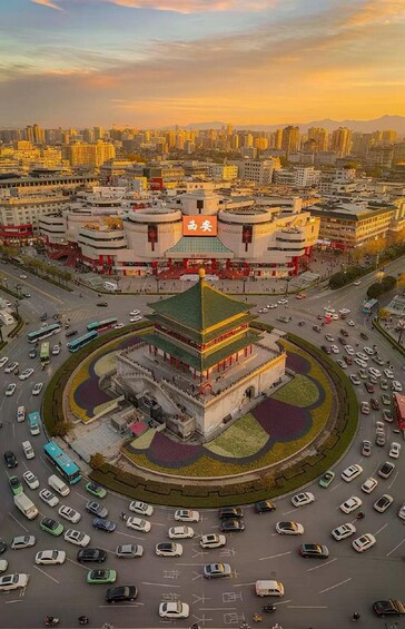 Une vue urbaine mettant en valeur un bâtiment traditionnel remarquable, doté d’un toit végétalisé, et entouré d’un rond-point où circulent des véhicules. 4