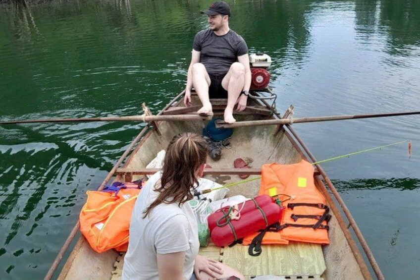 A small boat on calm water with a person sitting at the front and another person at the back. 1