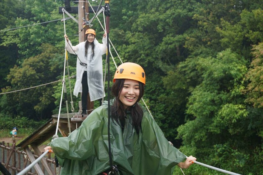Two people on a zip line course, wearing helmets and harnesses, with dense forest in the background. 4