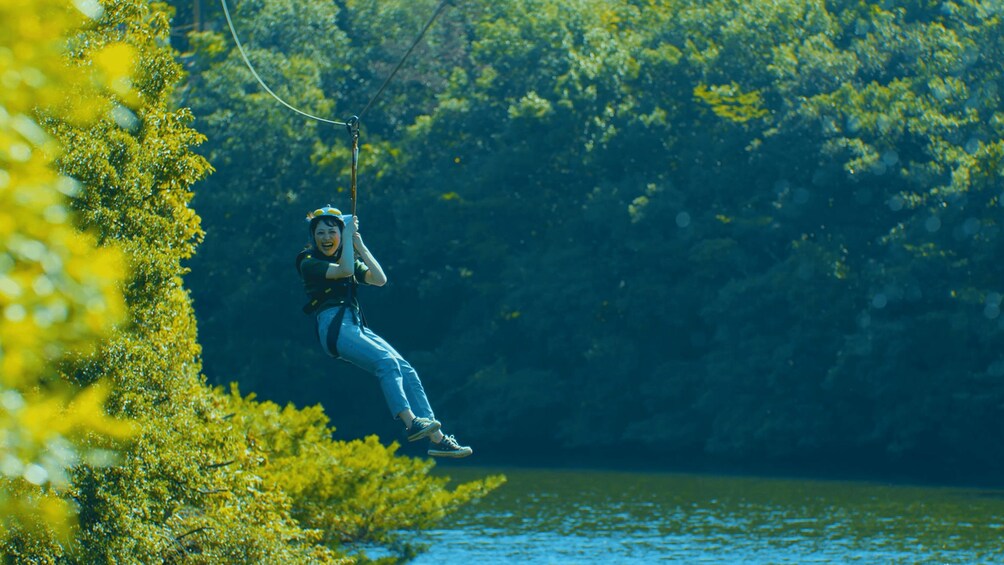 A person zip-lining over a forested area with a river below. 2