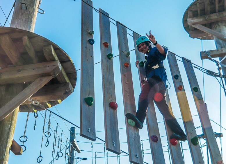 A person climbing a wooden obstacle course with various colored holds. 3