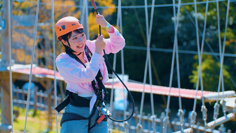 A person in a pink shirt and blue jeans wearing an orange helmet, holding onto a rope while suspended in the air. 1
