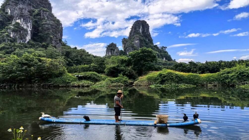 A person paddling a blue raft on a calm river surrounded by lush greenery and tall cliffs. 1