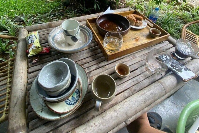 A wooden table with various dishes and drinks, surrounded by greenery. 2
