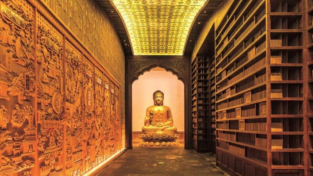 Une statue de Bouddha en or se trouve dans un couloir d’un temple, les murs étant ornés de sculptures complexes et des étagères remplies de livres. 3