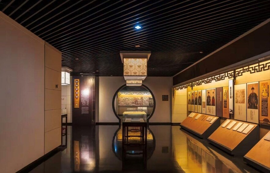 Un couloir de musée avec une vitrine centrale, des panneaux d’information et un plafond orné de motifs. 2