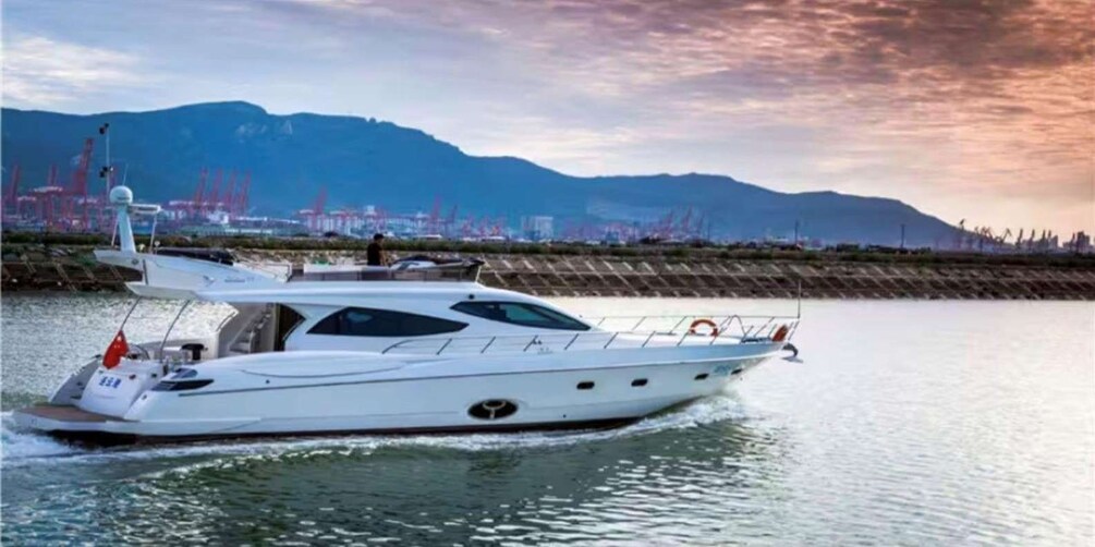 A white yacht on calm water with a mountainous backdrop and industrial structures. 3