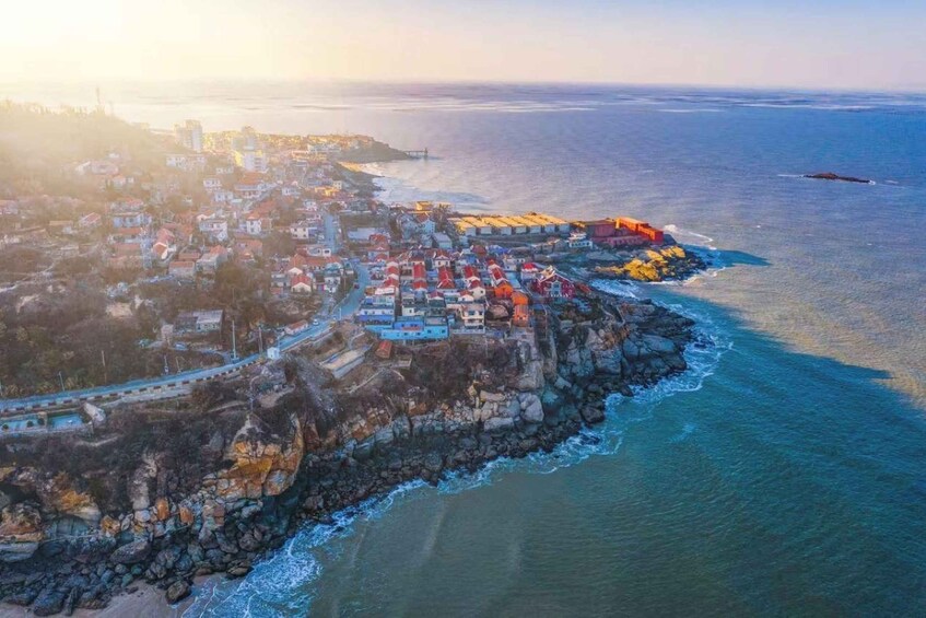 An aerial view of a coastal town with buildings along the shoreline, a bridge, and a clear view of the ocean. 1