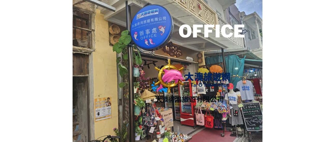 Une vitrine où sont exposés divers articles, notamment un panneau bleu avec du texte blanc, une décoration représentant un dauphin rose et une enseigne indiquant qu’il s’agit d’une boutique sur le thème de Hong Kong. 4