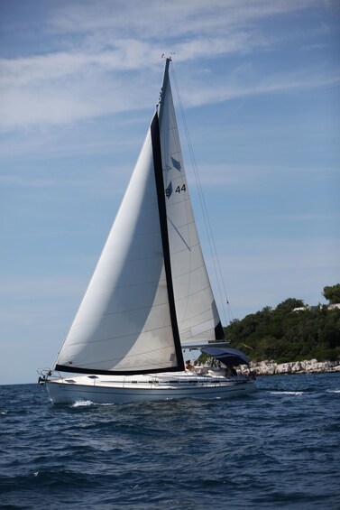 Eine Segelyacht mit weißem Segel und der Nummer 44 am Mast, die auf dem Wasser fährt. 1