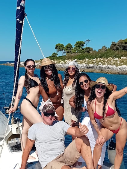 Eine Gruppe von Menschen auf einem Segelboot vor einer felsigen Küstenlinie mit Bäumen im Hintergrund. 2