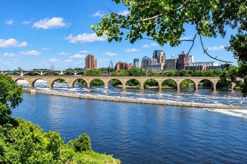 A river with a stone bridge, a city skyline in the background, and lush greenery in the foreground. 5
