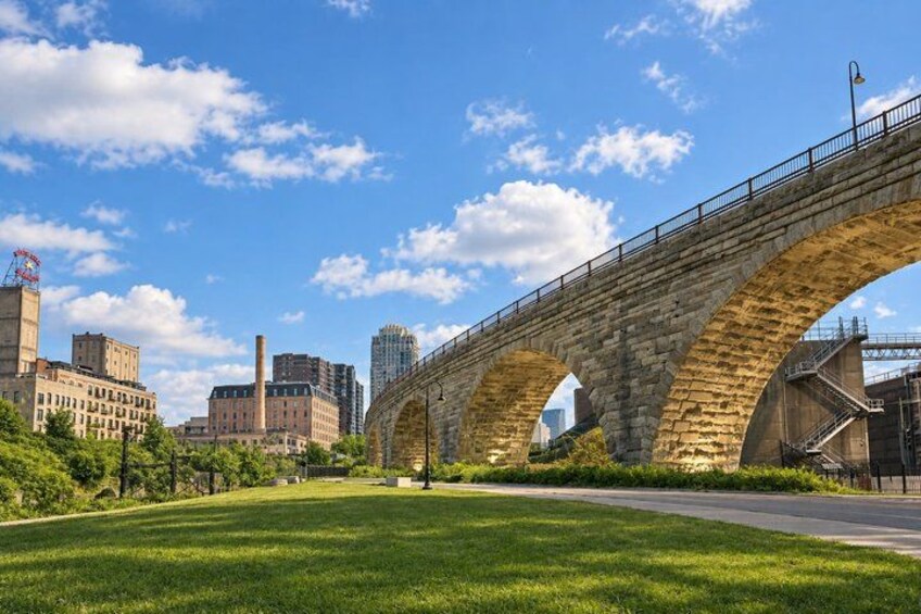 A stone bridge with multiple arches over a road, surrounded by greenery and buildings. 2