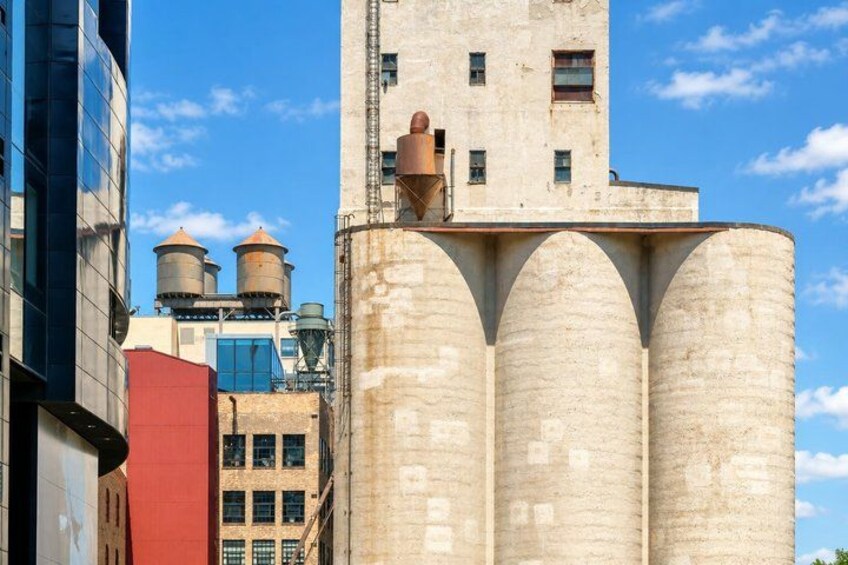 A grain elevator with large cylindrical structures, a modern building with reflective glass windows, and a red building in the foreground. 1