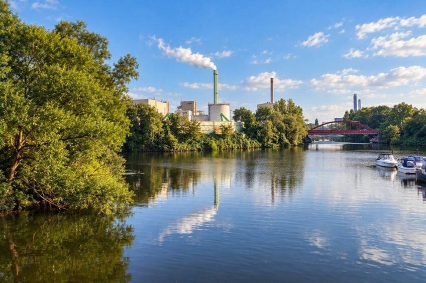 A calm river with boats, industrial buildings, and a red bridge. 3