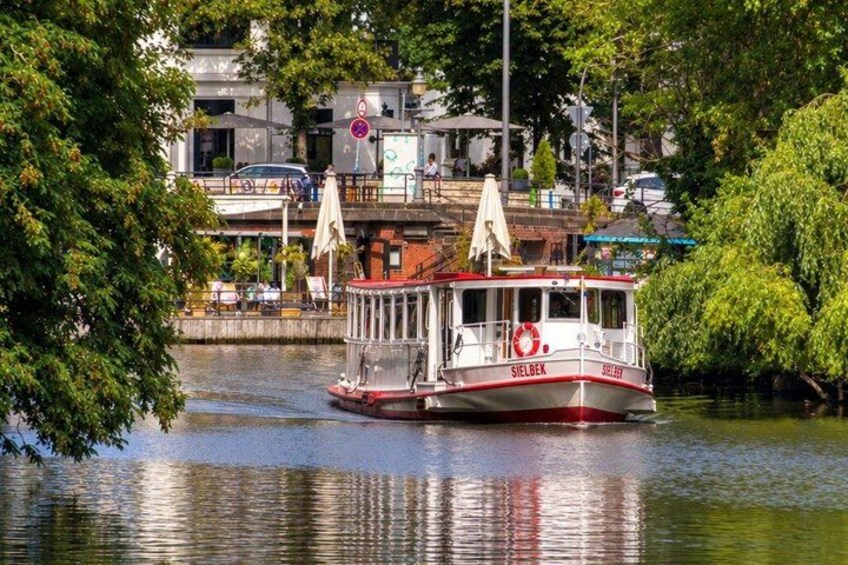 A riverboat named 'Sielgeck' on a calm river, surrounded by lush greenery and buildings in the background. 5