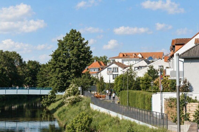 A riverside walkway with houses, a bridge, and a large tree. 4