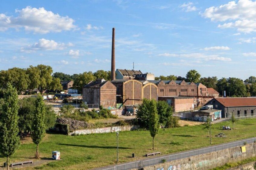 An industrial area with a tall chimney, brick buildings, and a grassy field. 2