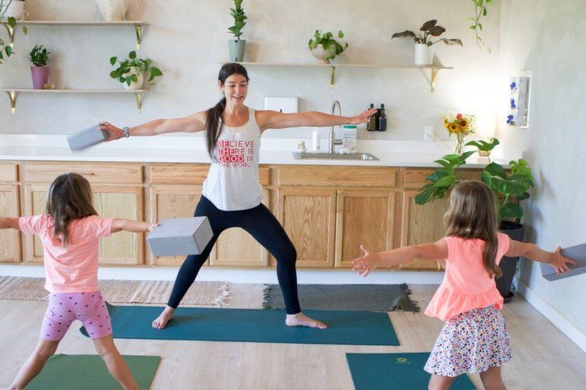 A woman and two children practicing yoga in a room with wooden cabinets and potted plants. 3