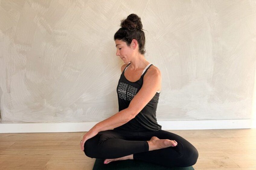 A person sitting cross-legged on a mat in a room with a plain wall and wooden floor. 2