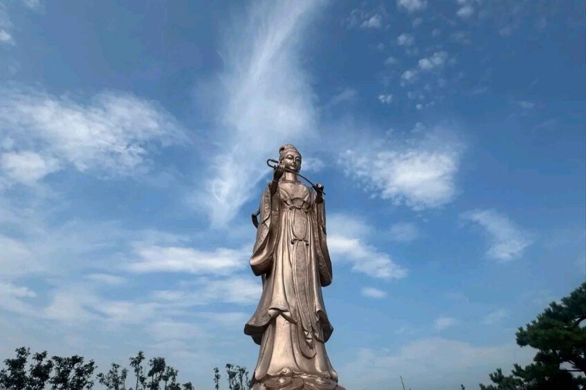 A statue of a woman in a flowing robe with a halo, standing against a clear sky with scattered clouds. 2