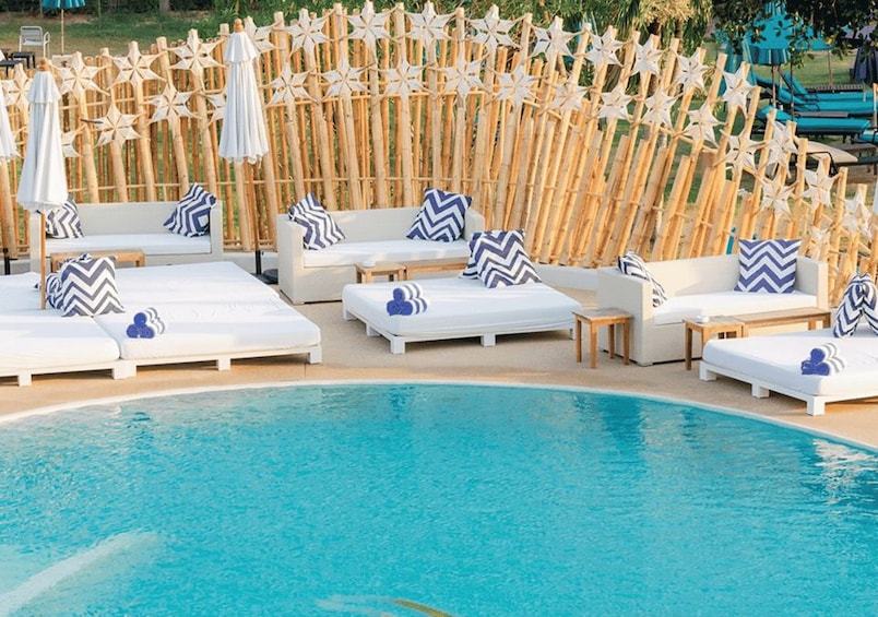 Un espace aménagé au bord de la piscine, avec des chaises longues blanches et des coussins à motifs bleus et blancs, le tout entouré d’une clôture en bambou ornée de décorations en forme d’étoiles. 5