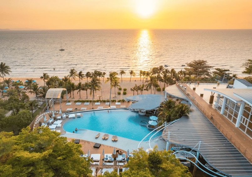 Un complexe hôtelier doté d’une piscine, de palmiers et offrant une vue sur l’océan au coucher du soleil. 1
