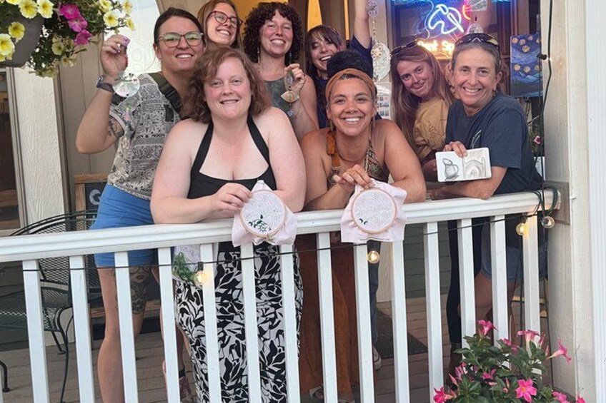 A group of people on a balcony with flowers and a neon sign in the background. 4
