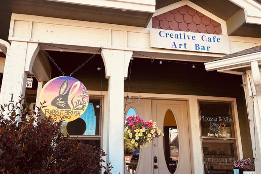 A building with a sign for 'Creative Cafe Art Bar' and another sign for 'Rabbit Brush Studio.' 1