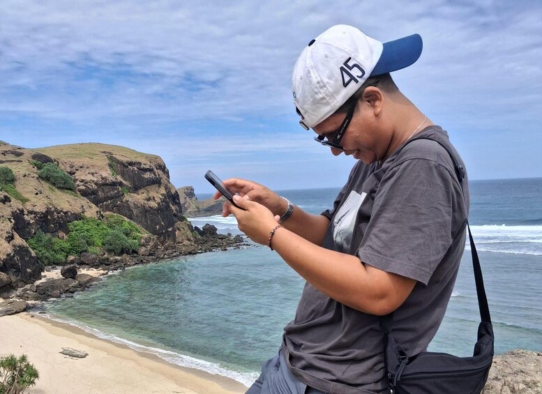 Eine Person benutzt ein Smartphone in Küstenlandschaft mit steilen Klippen und Strand. 5