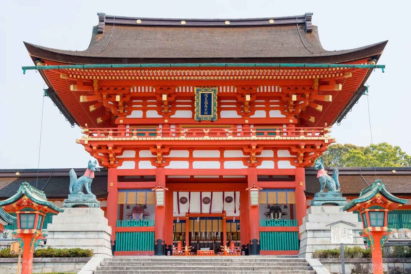 Un portón tradicional japonés con una combinación de colores rojo y verde, dos estatuas a cada lado y un letrero con caracteres japoneses. 1