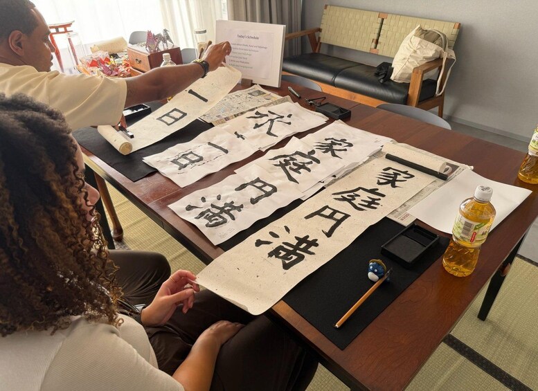 Une personne est en train d’écrire sur une grande feuille de papier avec des caractères japonais, une bouteille d’huile et un petit jouet bleu sont posés sur une table en bois. 4