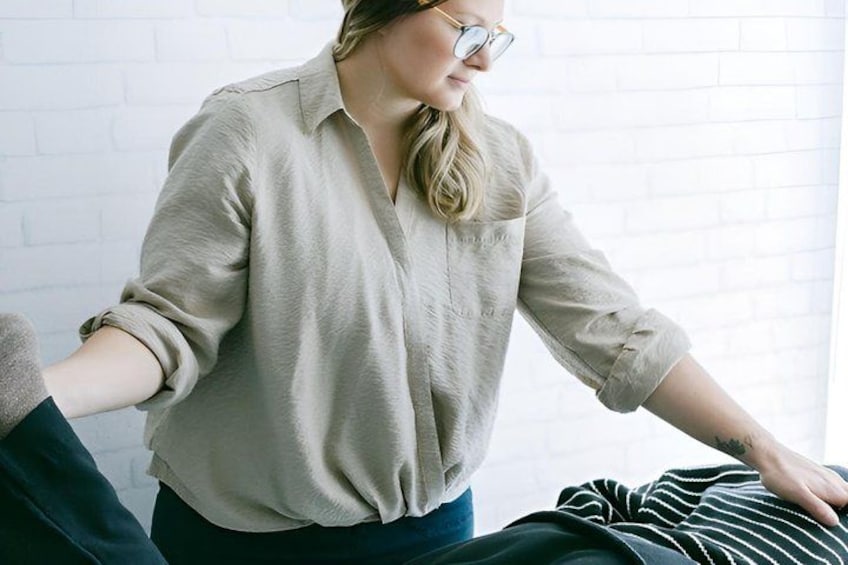 A person sitting on a bed with a striped blanket, wearing a beige shirt and dark pants. 1
