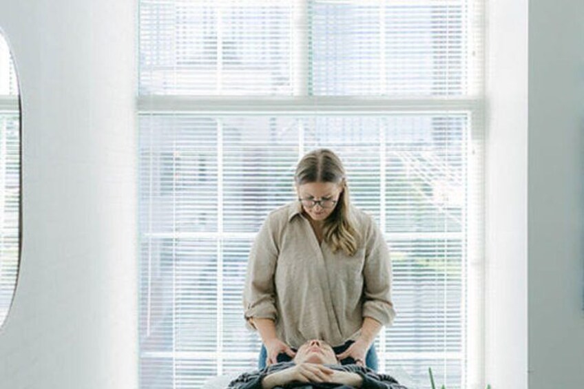 A person performing a massage on another individual in a room with large windows. 3