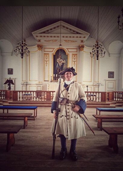 Une personne vêtue d’un uniforme militaire d’époque, se tenant dans une église à l’architecture riche et ornée, avec des bancs de prière. 4