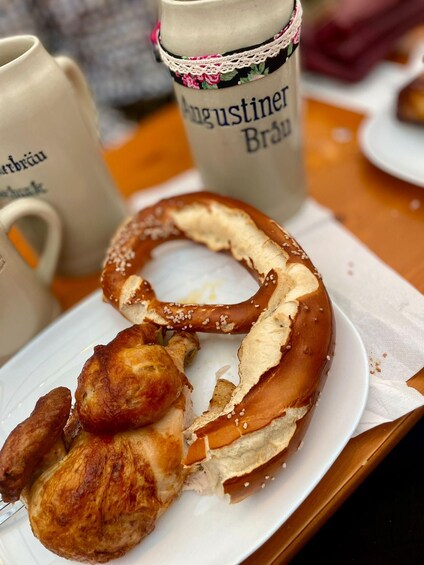 Un pretzel con una pata de pollo sobre un plato, una taza con diseño floral y un fondo desenfocado. 2