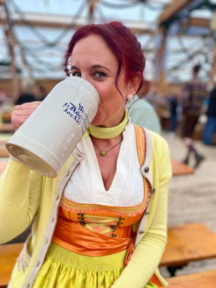 Una persona vestida con traje tradicional, sosteniendo una taza grande, sentada en una mesa al aire libre. 3